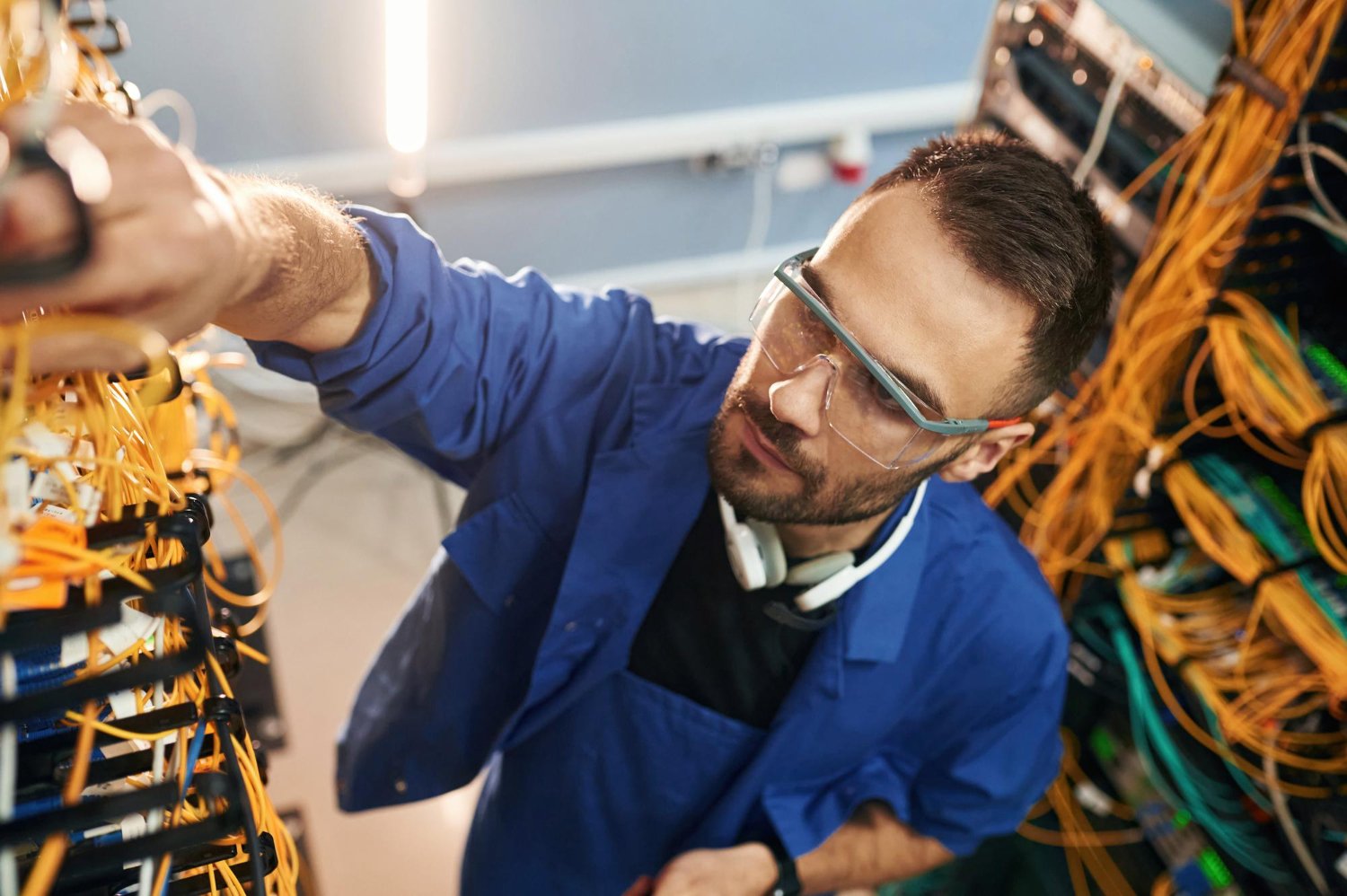 In blue colored uniform Young man is working with internet equipment and wires in server room